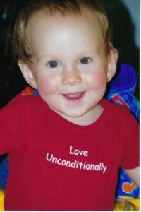 A young child wearing a red shirt with the words " love unconditionally ".