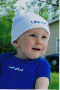 A baby wearing a hat with the word " unlimited " on it.